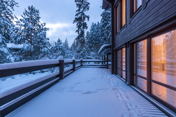 A wide terrace of a wooden house, illuminated from the inside, against the background of a...