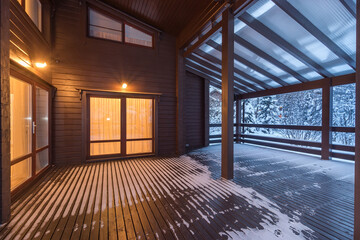 Light from the windows of the wooden house to the terrace under the canopy. Twilight. .Winter...