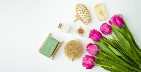 Obraz premium On a white background lie accessories for spa and beauty treatments, wooden brushes, aroma oils, fragrant handmade soap and a delicate, beautiful bouquet of tulips. Flat lay, top view.
