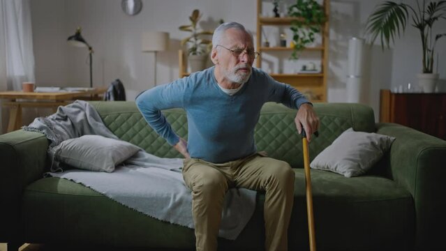 Mature male sitting on sofa and have cramps in lower back