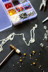 Box with colorful beads, string, wire, chain, scissors, pliers and hammer on dark background. Various jewelry making supplies. Selective focus.