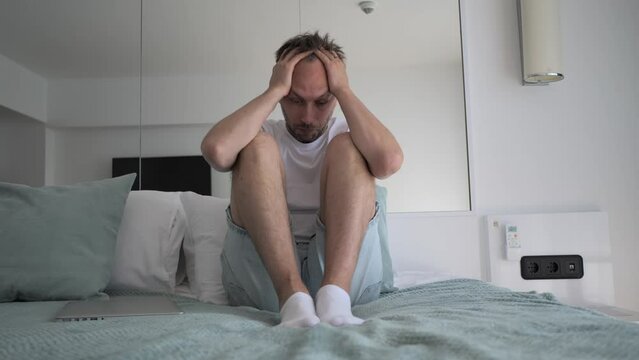 Stressed middle age man sits on bed holding head by hands. Portrait of person in problem life situation and depression.