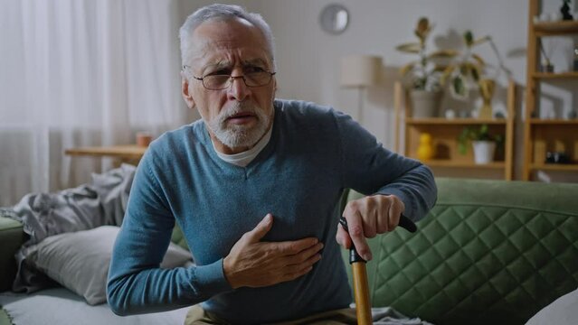 An elderly male with a heart attack is sitting at the couch in the living room