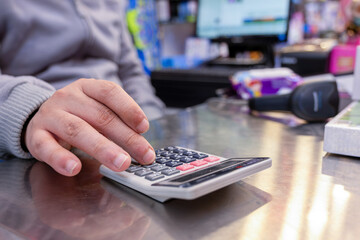 Cashier hands while calculating with barcode scanner and cashier drawer in the background