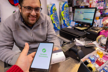 A man makes contactless payments at a bookshop or gift shop using his smartphone , seamlessly utilizing NFC or WiFi technology, without the need for physical touch