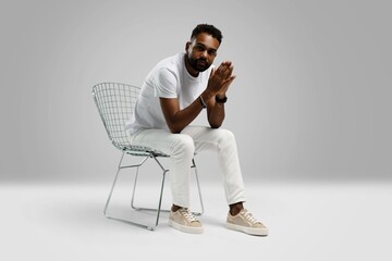Handsome young african american guy sitting on stool, posing in studio - isolated - obrazy, fototapety, plakaty