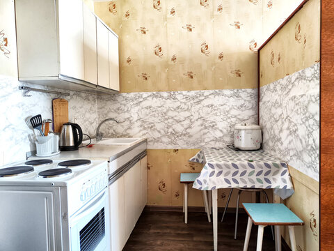 The interior is a small old kitchen with a table, stool, cabinets, sink and stove. Design in the Soviet poor outdated style