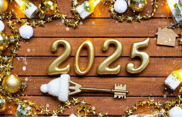 House key with tiny figure of home mock up on festive brown wooden background, lights of garlands. New Year 2025 wooden letters, greeting card. Purchase, construction, relocation, mortgage, insurance