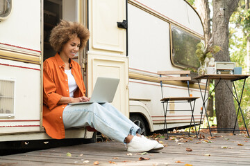 Young woman freelancer businesswoman working typing remotely on laptop computer while traveling alone in van camper home motor home trailer. E-learning concept - obrazy, fototapety, plakaty