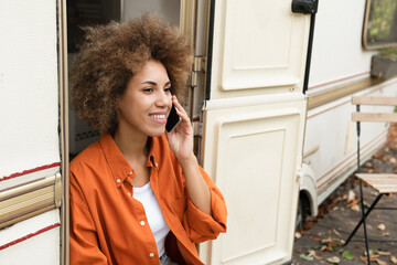 Happy african young traveler woman freelancer talking on phone smartphone with customers relatives...