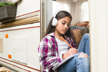 Small preteen learner girl daughter kid child listening to the music drawing doing homework while traveling trailer camper van wheel motor home trailer