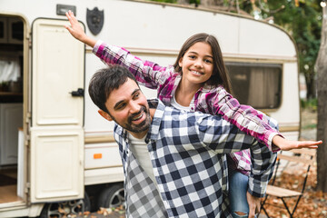 Preteen happy daughter kid child doing piggyback with father on a road trip voyage holiday by camper van wheel motor home trailer together. Happy Father`s day!