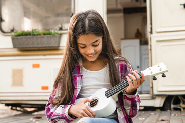 Small kid child daughter preteen girl playing ukulele while traveling driving by camper van...