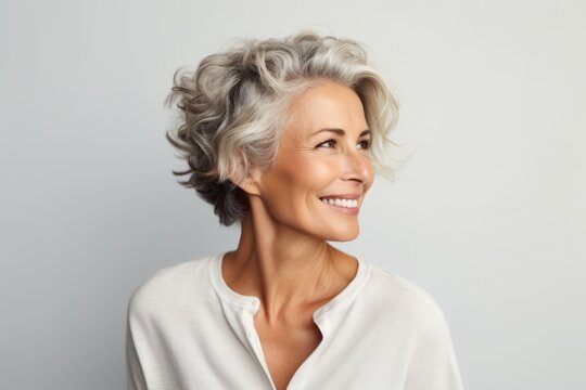 smiling senior woman with grey hair and white shirt on grey background