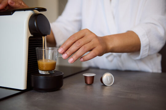 Close-up hands of housewife using a capsule coffee machine preparing freshly brewed espresso coffee in cozy home kitchen