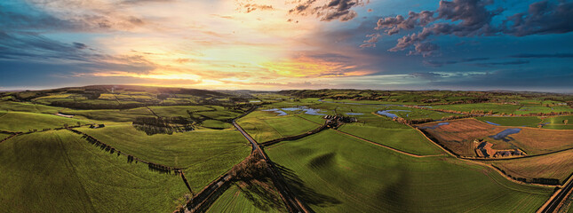 Panoramic view of a lush countryside at sunset with vibrant skies and rolling hills.