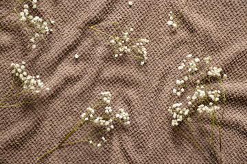 Brown soft crumpled bath towel and dry branches with small flowers as a background
