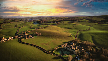 Aerial view of a picturesque rural landscape at sunset with rolling hills, a winding road, and a...