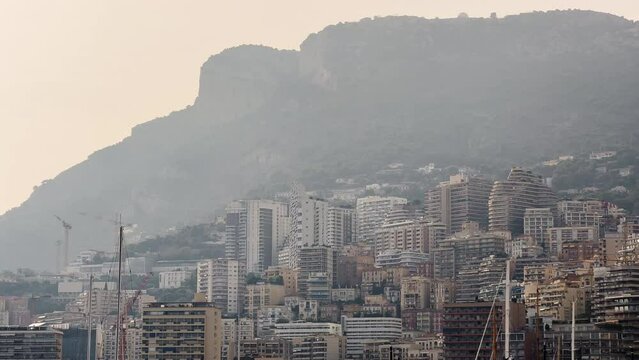 Residential complex of Monacoin the haze at sunset, buildings of different height against mountains, skyscrapers, clouds over city