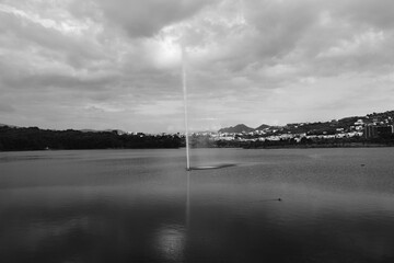 Tirana lake with a waterjet and breeze from a fountain, hills and green leafy trees on misty background.