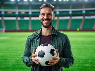 Handsome happy man with a soccer ball in his hands at the stadium