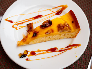 Piece of delicious pie covered with caramel and walnuts served in a ceramic plate on the table