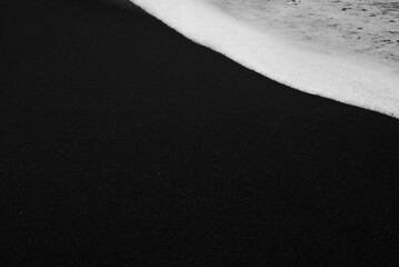 Mostly blurred black sand beach with white foam of sea waves background