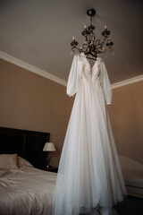 The image features a wedding dress hanging on a hanger in a bedroom. 5246