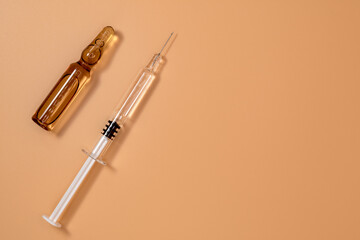 Small full syringe with needle on peach background. Next to it is the vial of medicinal liquid (small brown ampoules). Copy Space.