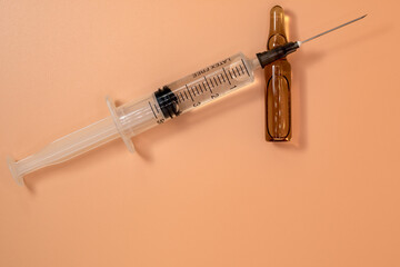 Full 5ml syringe with needle on peach background. Next to it is the vial of medicinal liquid. Copy Space.