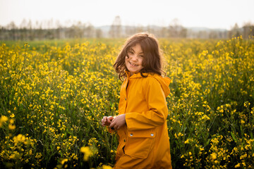 Naklejka na ściany i meble smiling girl in yellow raincoat standing in a blooming field