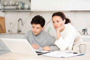 Boy studiyng using laptop, mother helping and explaining