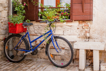 Fototapeta na wymiar bicycle with a basket near a wall with a window with open shutters and red fresh homemade flowers in pots