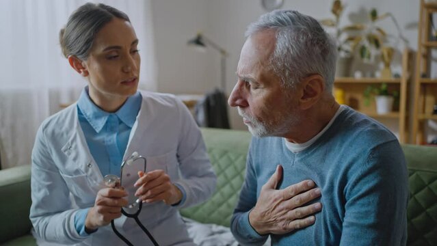Smiling female doctor using stethoscope to listen senior elderly patient heartbeat