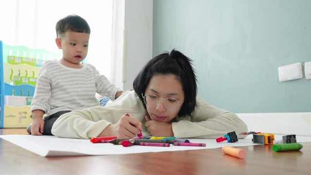Asian Mother and little son drawing and coloring with Crayons. Woman and little child boy enjoy painting with Crayons on paper together.