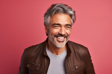 Portrait of a smiling mature man in a leather jacket on a pink background.