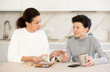 Mother giving some cash and instructions her teenager son sitting at home in kitchen