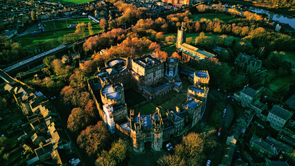 Aerial view of a historic Lancaster castle at sunset with surrounding greenery and roads.