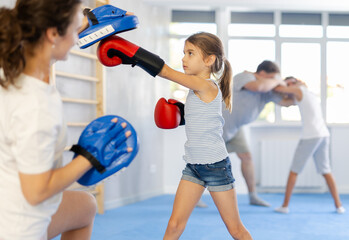 Mother and girl are engaged during training, boxing classes. Parent helps daughter master basic...