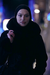 Muslim woman walking on an urban city street on a cold winter night wearing hijab