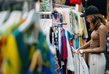 Teenage girl choosing a clothes at the evening bazaar. - obrazy, fototapety, plakaty