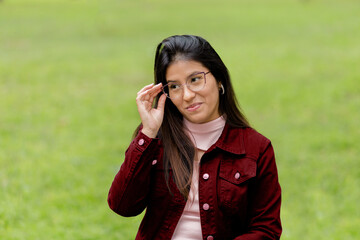 Close-up portrait of a young and beautiful woman with glasses, looking suspiciously at the camera against a green pasque background. Concept of human emotions, facial expression, advertising