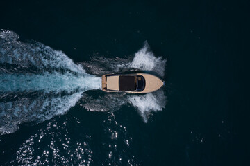 Large high-speed modern wooden boat with people moving fast on dark water, top view.