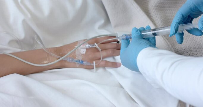 Male doctor in gloves injecting drip of biracial female patient in bed with syringe, slow motion