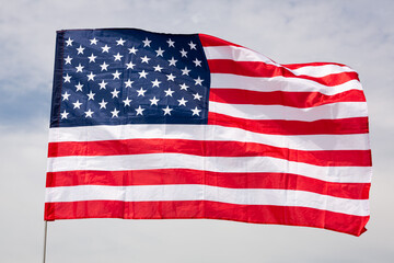 Flag of United States with horizontal stripe of red and white, fifty five-pointed stars in blue rectangle, representing fifty states, symbolizing American unity waving on flagstaff against cloudy sky