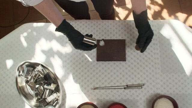 Woman confectioner works with metallic molds to create different shapes of chocolate candies. Woman transforms basic ingredients in confections