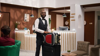 African american bellboy takes suitcases to help important guest with room accommodation, providing...