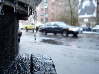 Close up of a black fire hydrant covered with ice with an out of focus car in the background in New...