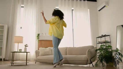 Dancing funny African American woman young beautiful curly hair girl jumping at apartment ethnic joyful female lady dance to music happy life exciting good mood having fun vacations weekend home party