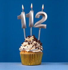 Burning candle number 112 - Birthday card with cake on blue Background